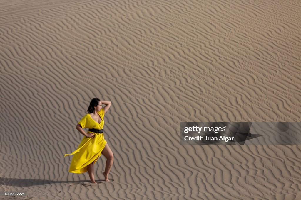 Photo with copy space of a woman in a yellow summer dress posing barefoot in the desert