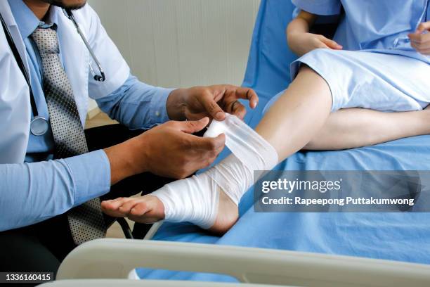 doctor putting bandage on injured feet of patient in hospital - mullbinde stock-fotos und bilder