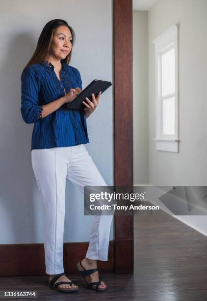young woman standing indoors using digital tablet - blue shoe foto e immagini stock