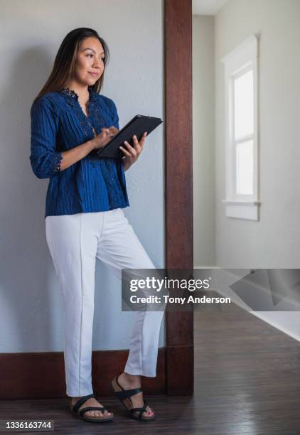 young woman standing indoors using digital tablet - blue blouse stock pictures, royalty-free photos & images