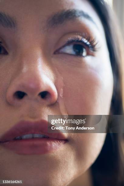 close up of young woman's face with tear running down her cheek - teardrop stockfoto's en -beelden