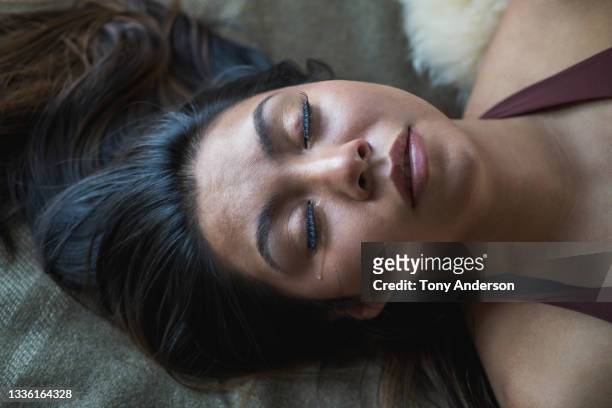 young woman lying on bed with tear running down her cheek - crying woman stock-fotos und bilder