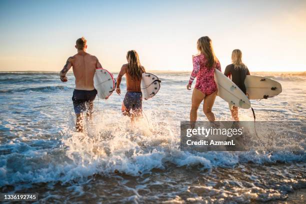 surfers with boards running into water at burleigh heads - burleigh beach stock pictures, royalty-free photos & images