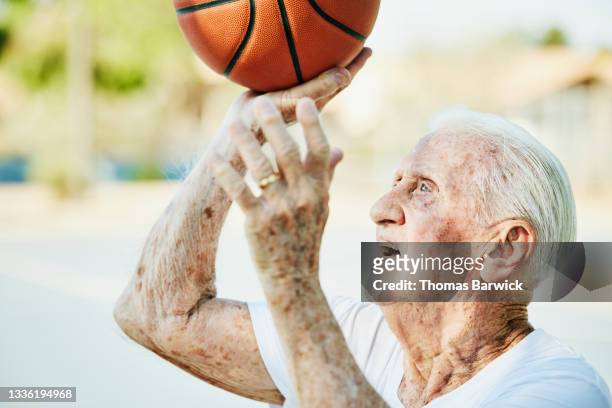 Medium close up shot of senior man taking shot on outdoor basketball court on summer morning