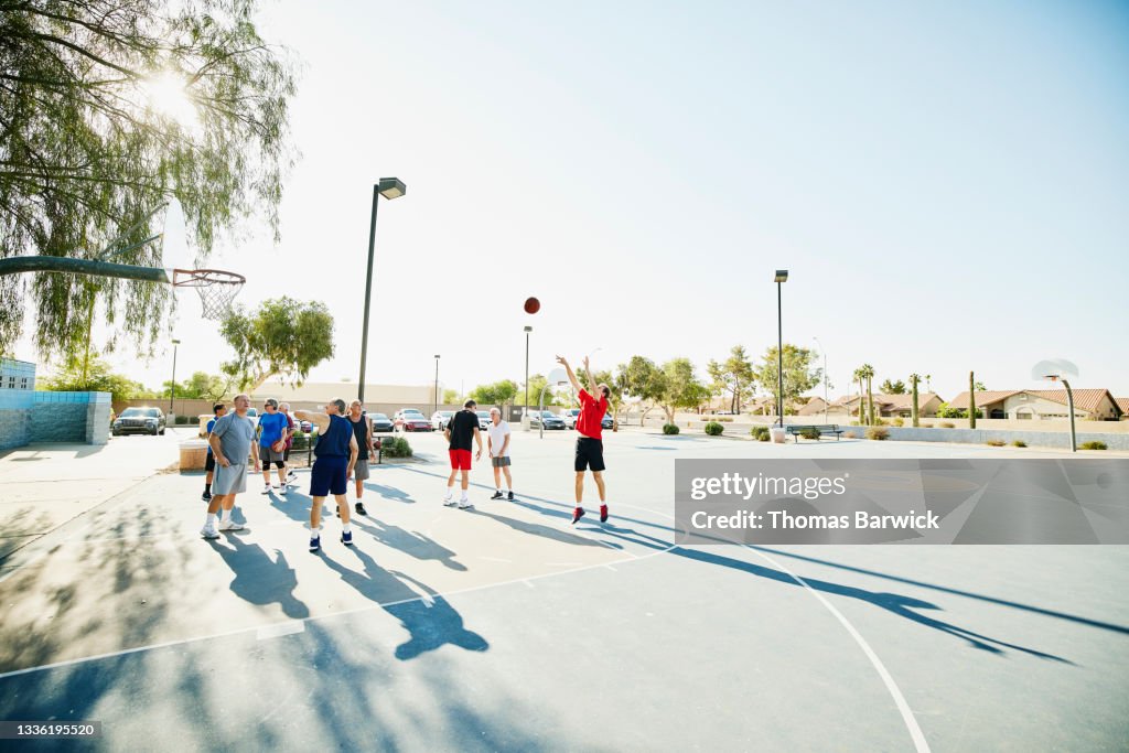 Extreme wide shot of senior men warming up before basketball game on summer morning