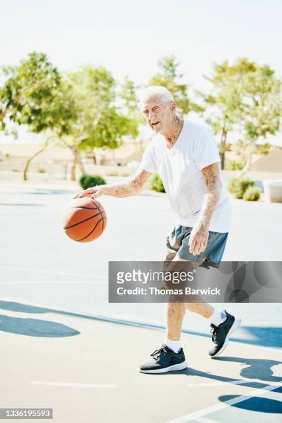 Wide shot of senior smiling man dribbling basketball during game on summer morning