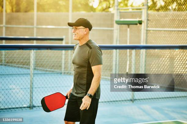 medium shot of senior man on pickleball court while playing match on summer evening - schlägersport stock-fotos und bilder