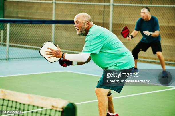 Wide shot of senior man playing at net during doubles pickleball match