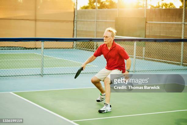 Wide shot of senior man approaching net while playing pickleball on summer evening