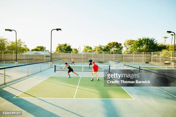 Extreme wide shot of senior friends playing doubles pickleball on sunny summer evening