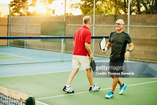 Wide shot of smiling senior man playing doubles pickleball on summer evening