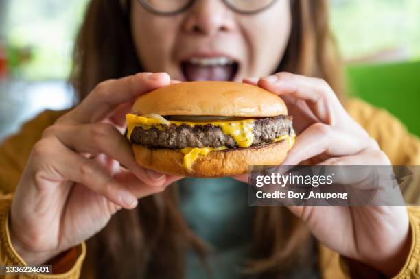 close up of woman opened her mouth to eat a classic beef cheeseburger. - adults eating hamburgers stock-fotos und bilder