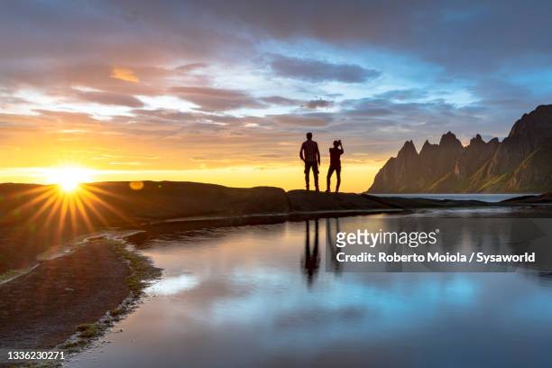 hikers photographing midnight sun with smartphone, norway - senja stockfoto's en -beelden