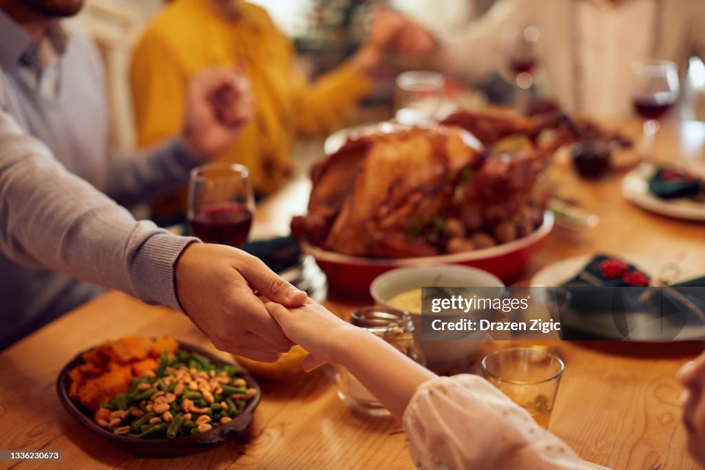 Close-up of father and daughter praying during family meal on Thanksgiving at dining table.