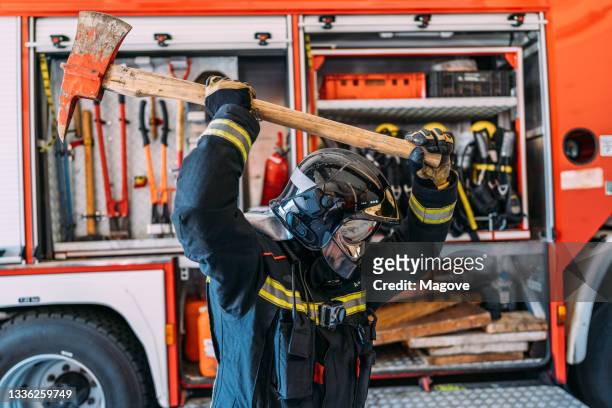 a firefighter in uniform demonstrating how he uses his axe as part of his tool of the trade - fireman axe stock pictures, royalty-free photos & images