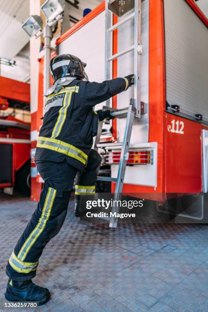 firefighter climbing up the back stairs of the fire truck - brandweerkazerne stockfoto's en -beelden
