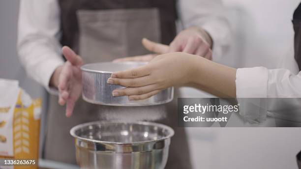 young asian couple sifting flour in bowl - sifting stockfoto's en -beelden