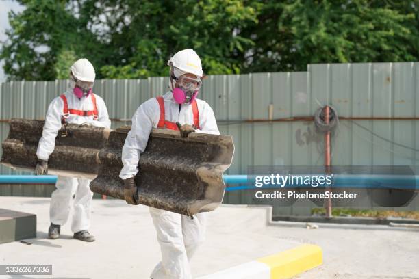 safety is our top priority. workers wearing full body protective clothing while working with the asbestos roof tiles. - asbestos removal photos et images de collection