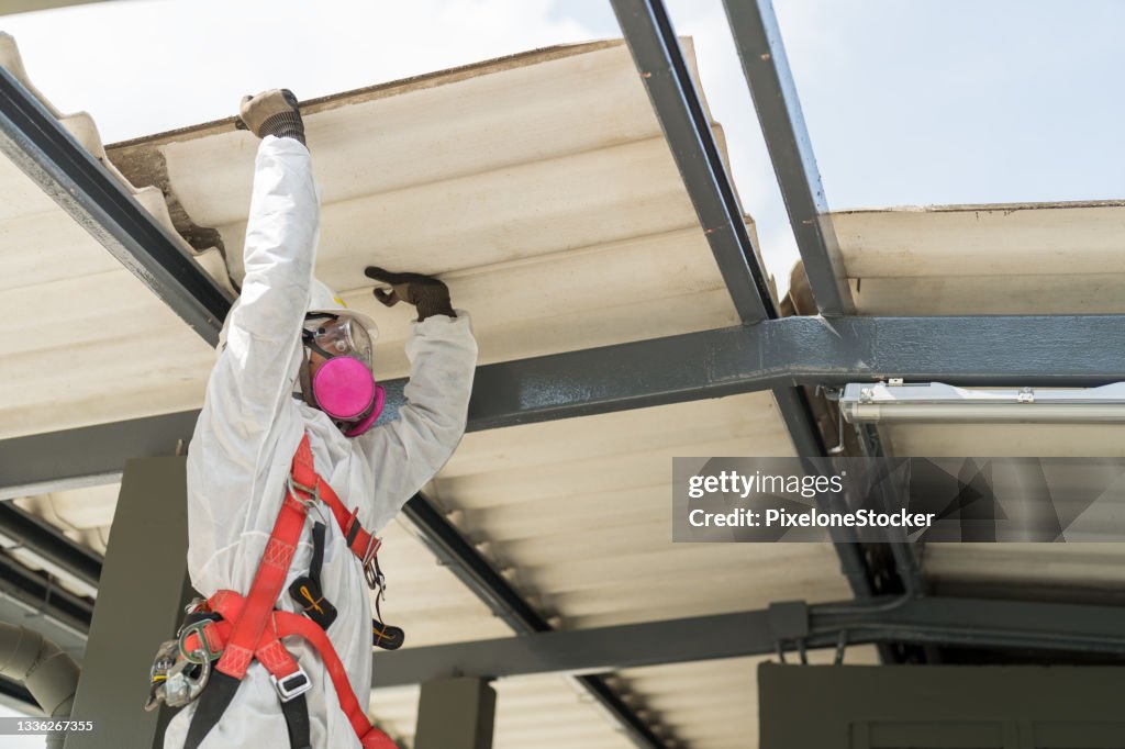 Safety is our top priority. Worker wearing full body protective clothing while working with the asbestos roof tiles.