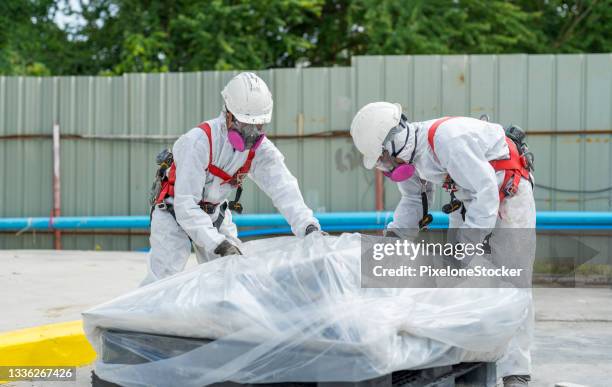 safety is our top priority. workers wearing full body protective clothing while working with the asbestos roof tiles. - asbestos removal photos et images de collection