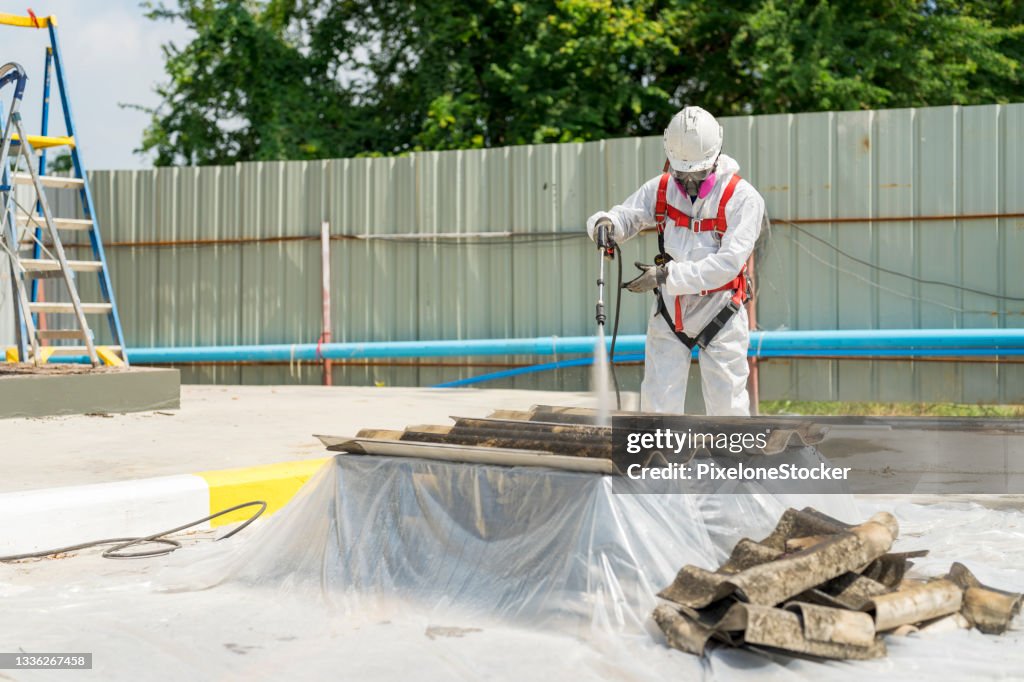Safety is our top priority. Worker wearing full body protective clothing while working with the asbestos roof tiles.