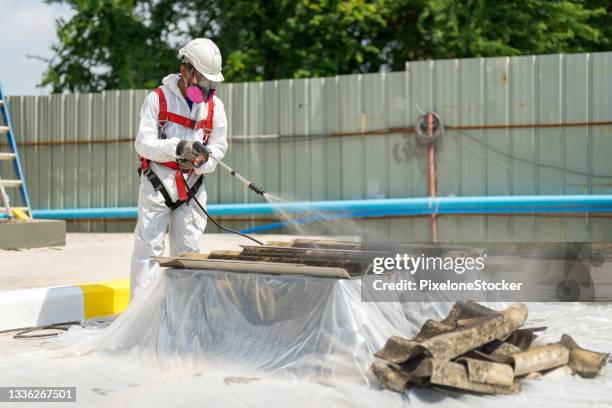 safety is our top priority. worker wearing full body protective clothing while working with the asbestos roof tiles. - asbestos removal photos et images de collection