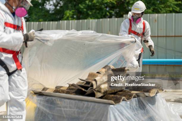 safety is our top priority. workers wearing full body protective clothing while working with the asbestos roof tiles. - asbestos stock pictures, royalty-free photos & images