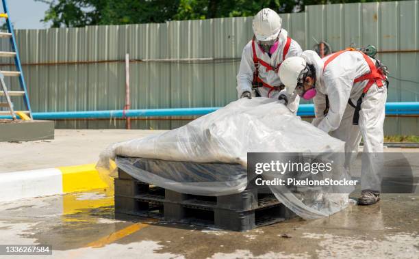 safety is our top priority. workers wearing full body protective clothing while working with the asbestos roof tiles. - asbestos removal photos et images de collection