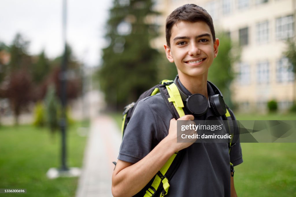 Portrait of smiling teenage boy in front of the school