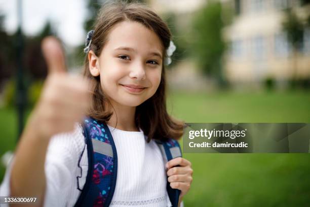 cute smiling happy schoolgirl gesturing thumb up in front of the school - goodbye single word stock pictures, royalty-free photos & images