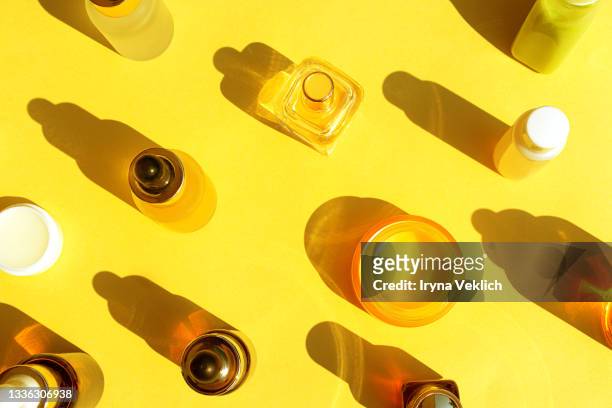 trendy beauty concept with facial serum, natural essential oil, hand cream, lip balm and perfume in cosmetic bottles with dropper and bright sunny shadow on yellow color background. - korean beauty products foto e immagini stock