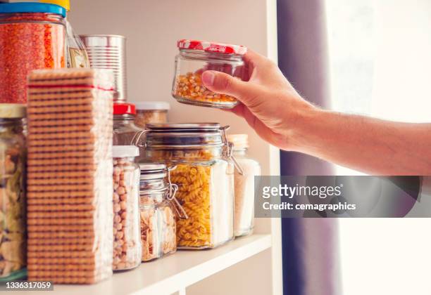 a man takes or places glass jars filled with legumes from a shelf in the pantry - food staple stock pictures, royalty-free photos & images