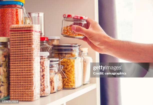 a man takes or places glass jars filled with legumes from a shelf in the pantry - kitchen pantry bildbanksfoton och bilder