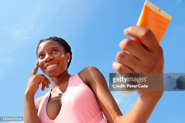 woman applying sun cream to face - sunbathing stock pictures, royalty-free photos & images