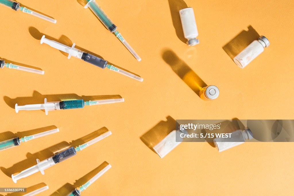 Syringes are filled with injection and medical vaccine bottles on a yellow background. Flat lay
