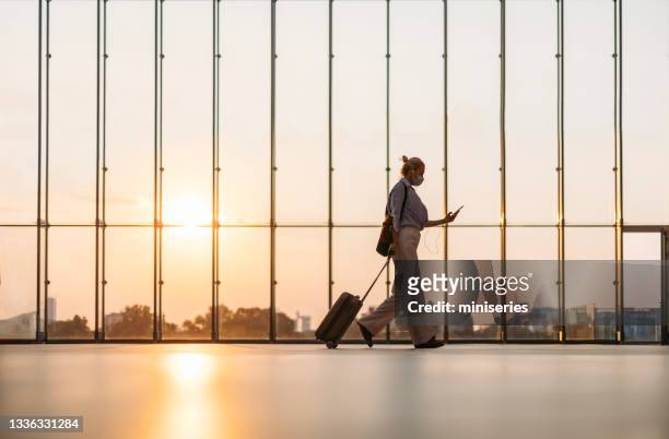 business woman using mobile phone at the airport - woman blond looking left window stockfoto's en -beelden