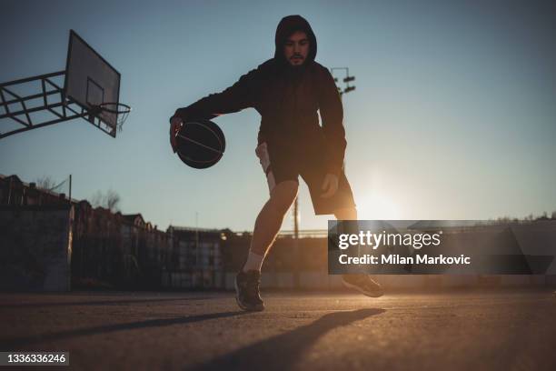 der junge mann trainiert allein auf dem basketballplatz. - streetball stock-fotos und bilder