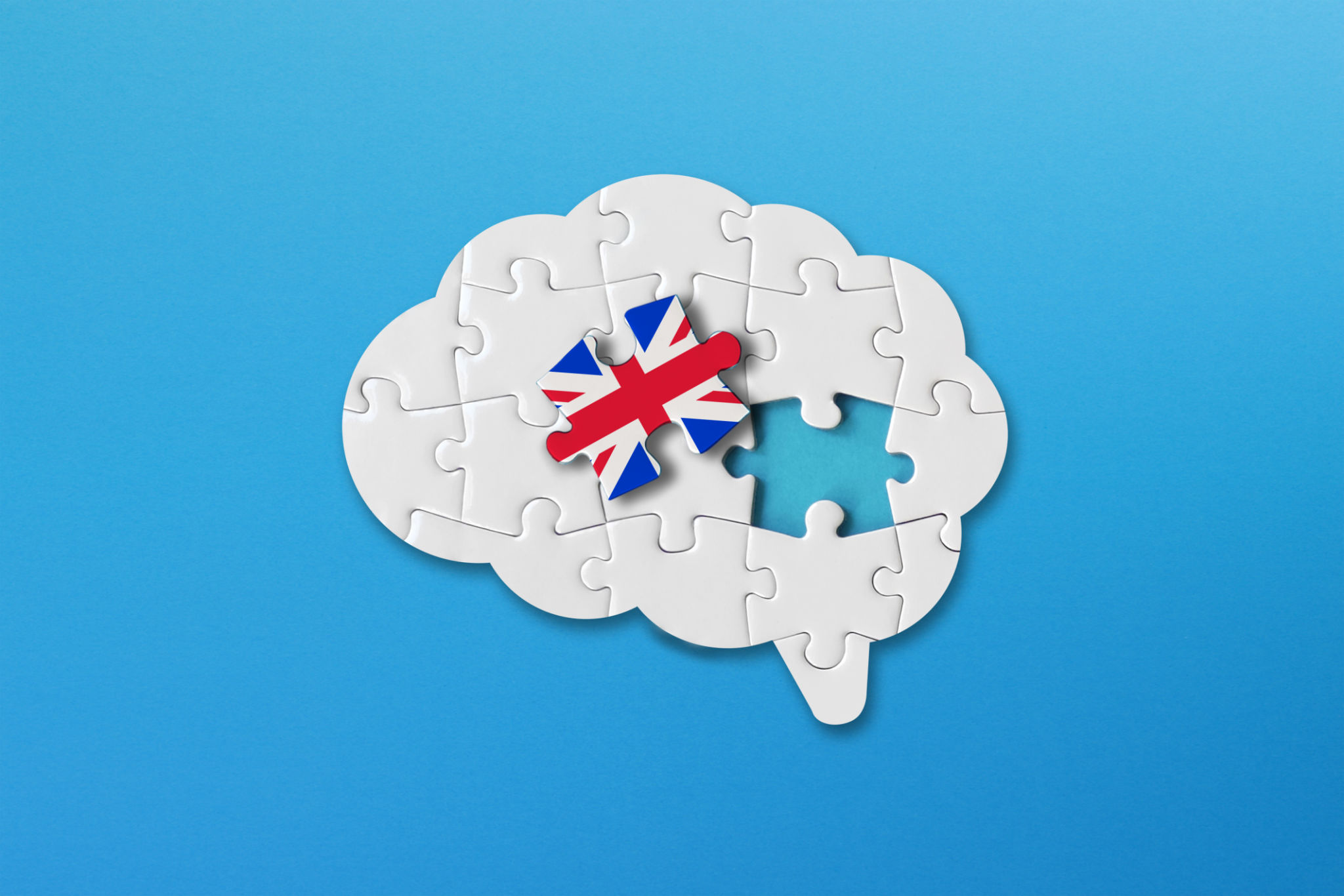 English learning concept, white jigsaw puzzle pieces with british flag a human brain shape on blue background English learning concept, white jigsaw puzzle pieces with british flag a human brain shape on blue background