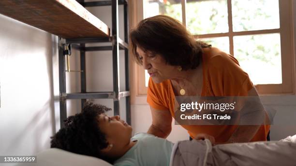 grandmother putting granddaughter to sleep at home - kids sleep in bed stockfoto's en -beelden