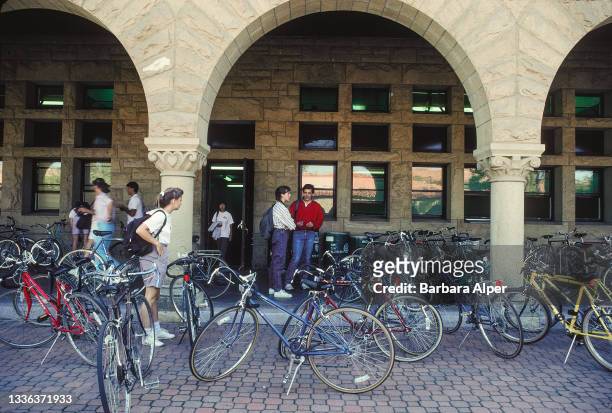 View of parked bicycles, and several students, in front of a building on the Stanford University campus, Stanford, California, October 1989.
