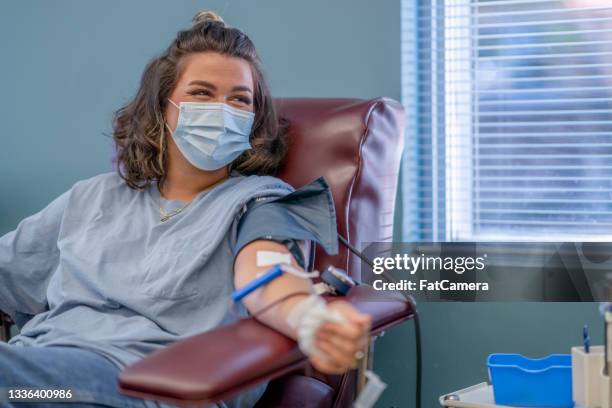 mujer joven enmascarada feliz de estar donando sangre - blood donation fotografías e imágenes de stock