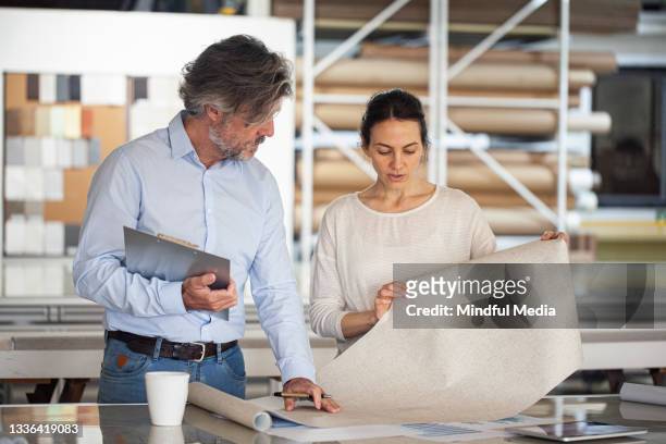 sustainable designer sharing ideas with colleague inside textile factory - corporate social responsibility stock pictures, royalty-free photos & images