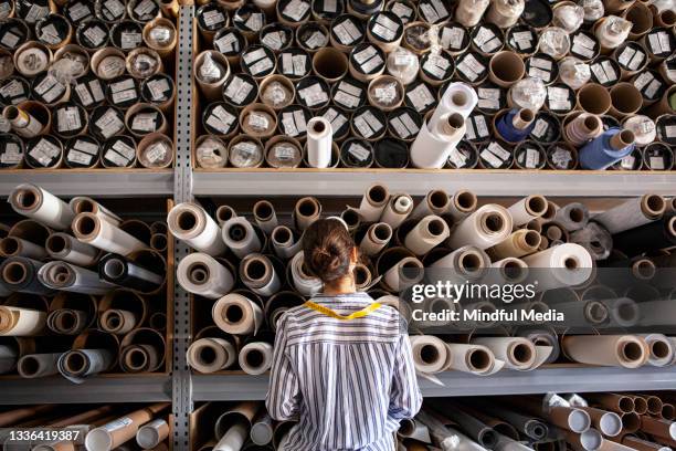 portrait d’un designer textile choisissant un tissu à partir d’une pile de rouleaux à l’intérieur d’un atelier durable - industrie textile photos et images de collection