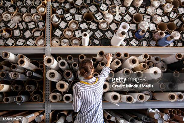 portrait d’un designer textile choisissant un tissu à partir d’une pile de rouleaux à l’intérieur d’un atelier durable - fabric rolls photos et images de collection