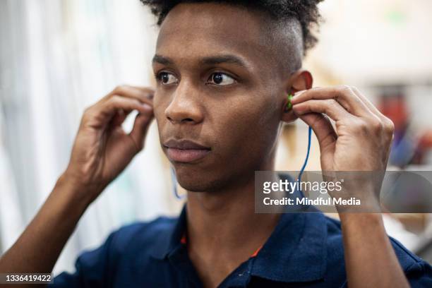portrait of industrial laborer wearing safety earplugs while standing indoors at workplace - ear plug stock pictures, royalty-free photos & images