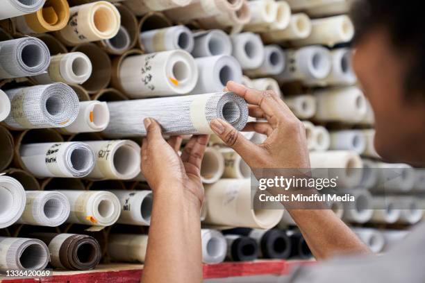 créatrice de mode souriante choisissant des tissus à partir de rouleaux d’échantillons textiles à l’intérieur de l’usine - fabric rolls photos et images de collection