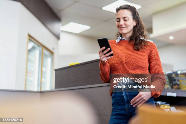 vista de ángulo bajo de mensajes de texto de mujeres adultas jóvenes mientras está de pie dentro de la tienda de la estación de servicio de combustible - mujer feliz sola 30 35 fotografías e imágenes de stock