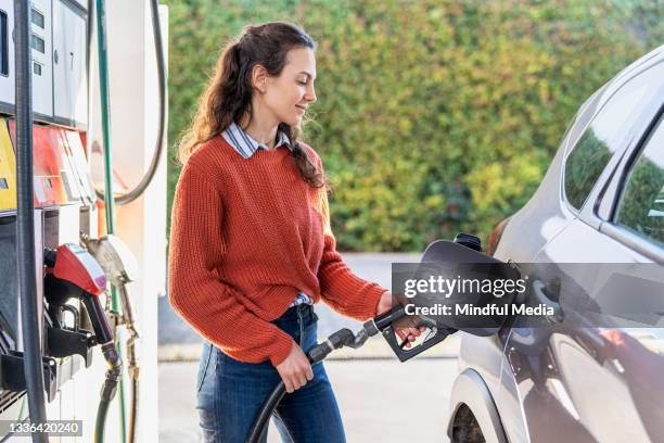 side view of young adult woman filling fuel tank while standing next to car - refuelling stock pictures, royalty-free photos & images