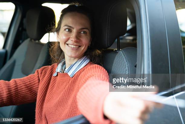 retrato de una clienta sentada en el asiento del conductor entregando la tarjeta de crédito - mujer feliz sola 30 35 fotografías e imágenes de stock