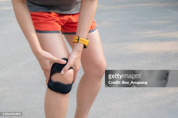 cropped shot of runner woman holding her knee while she having suffering from knee pain and she wearing knee braces for supports to be worn when you have pain in your knee. - itb stock pictures, royalty-free photos & images